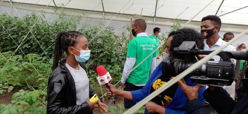 Student wearing mask talking in front of a media camera and journalist during the tree planting campaingn